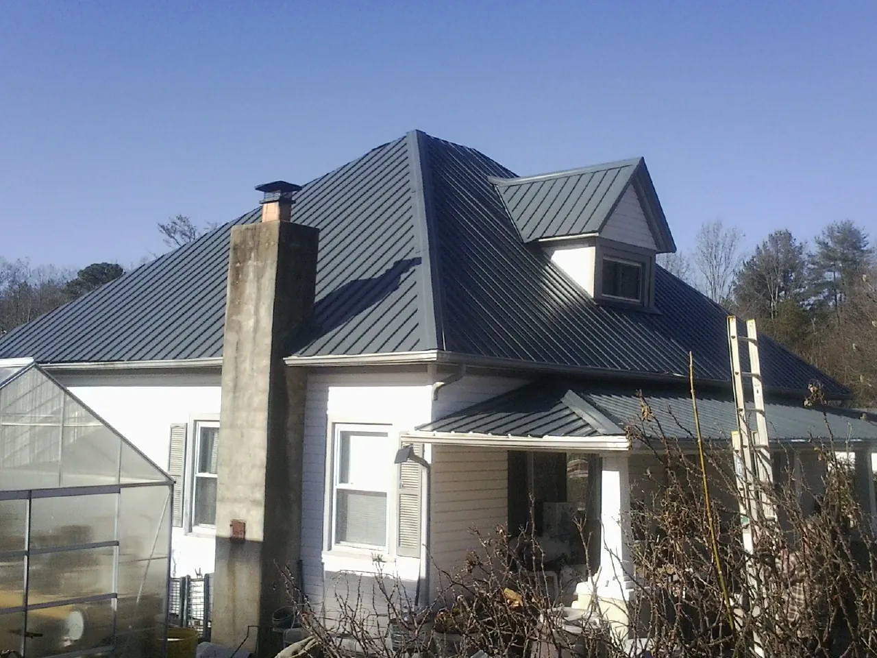 Dark blue standing seam metal roof on a white farmhouse with dormer — Slate & Tile Roof Repair by Roofing Brothers in Kaleva