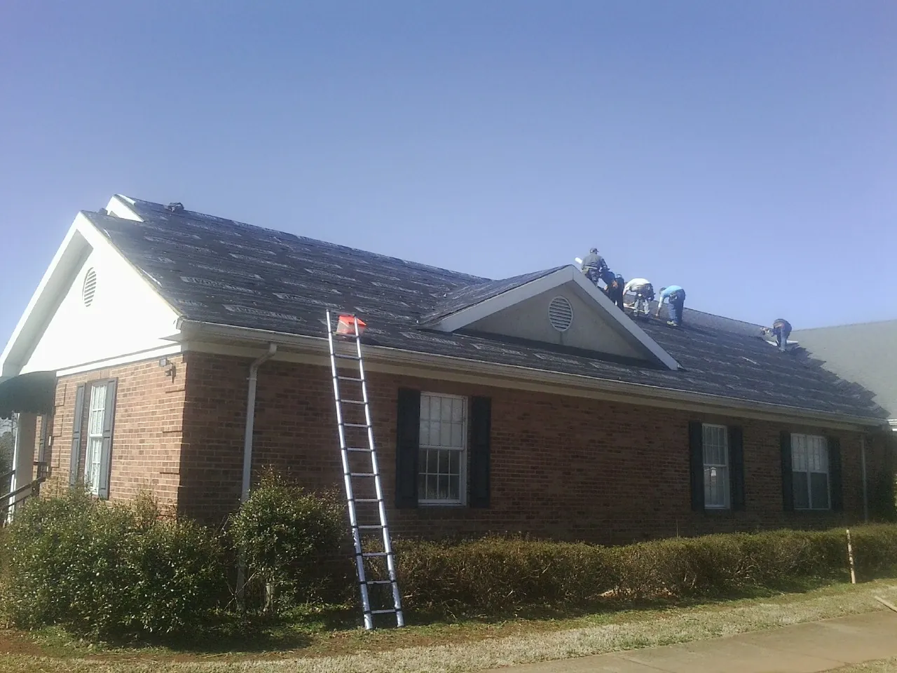 Crew tearing shingles off a brick ranch roof with a ladder set — Emergency Roof Repair work by our crew in Kaleva