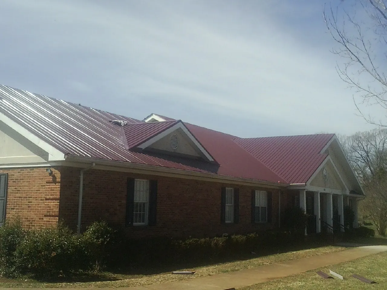 Red metal roof with gabled entries on a long brick building, from a Hail Damage Roof Repair job in Kaleva