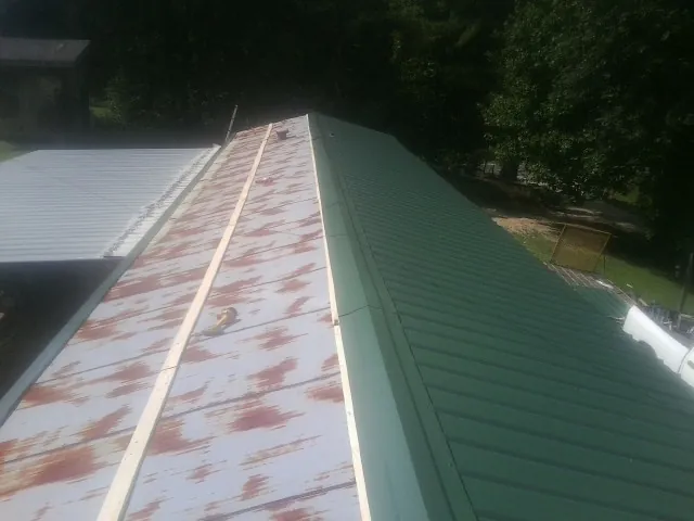 Old rusted panels beside newly installed green metal roofing — Wind Damage Roof Repair by Roofing Brothers in Kaleva