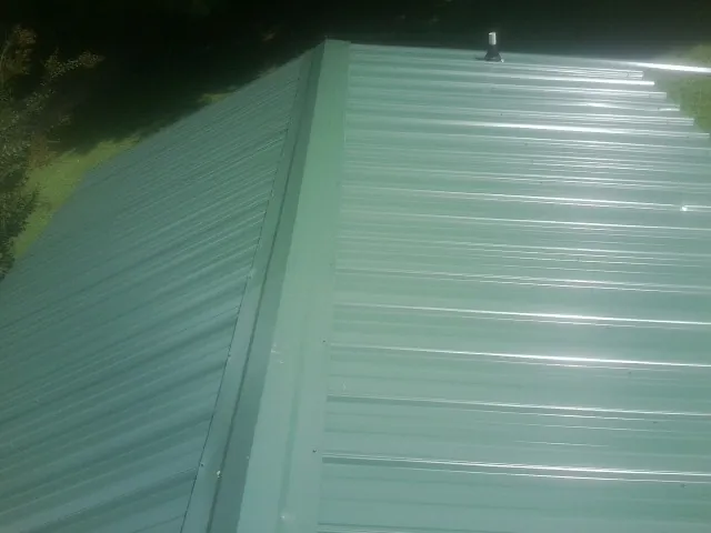 New green metal panels meeting at the ridge of a roof — Flat Roof Repair work by our crew in Kaleva
