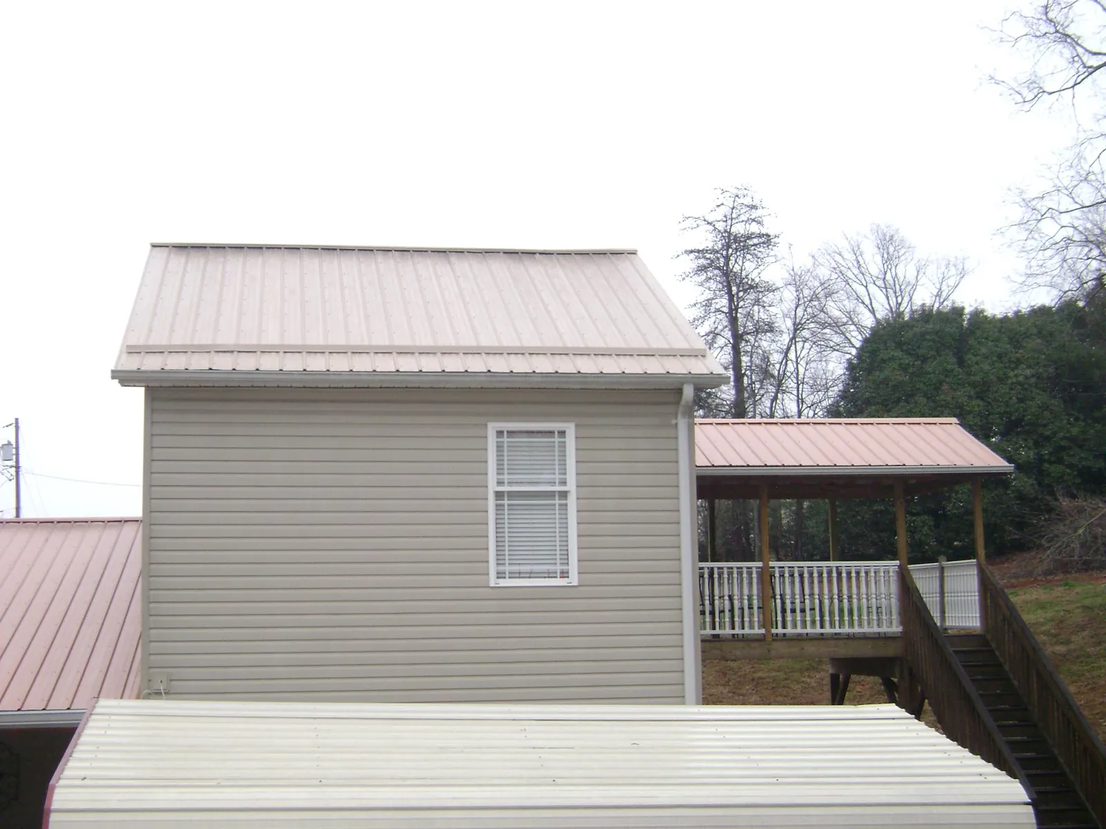 Tan metal roofs on a two story addition and attached porch, from a Roof Replacement job in Kaleva